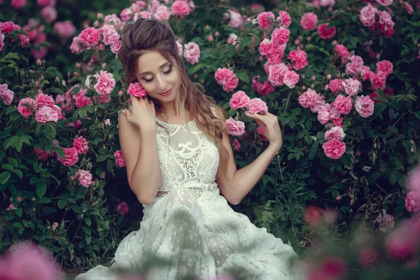 Vacker kvinna i en blomsterpark, trädgård rosor. Makeup, hår, en krans av rosor. — Stockfoto