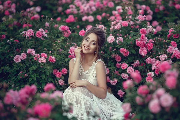 Bella donna in un parco floreale, rose da giardino. Trucco, capelli, una corona di rose . — Foto Stock