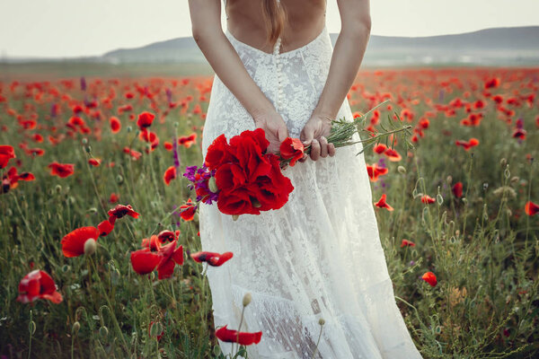 Beauty woman in poppy field in white dress. Beautiful bride in Boho style at sunset in a field of red poppies