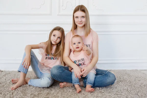 Leichte Familienserien. drei Schwestern auf weißem Hintergrund, bekleidet mit lustigen T-Shirts und Jeans — Stockfoto