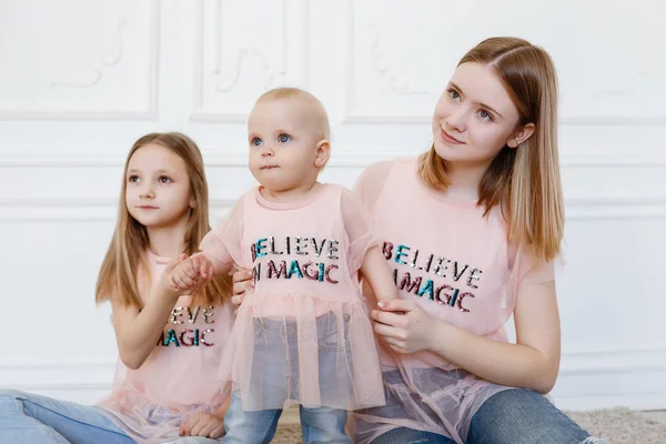 Lichte familie serie. Drie zussen op een witte achtergrond, gekleed in grappige t-shirts en jeans — Stockfoto