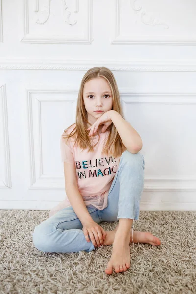Cute pre-teen girl wearing fashion clothes posing in white interior