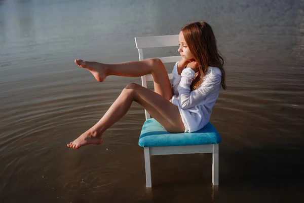Una hermosa niña pequeña en una silla en medio de un estanque . — Foto de Stock
