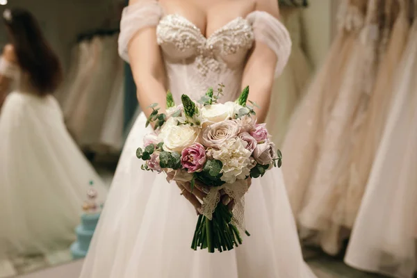 Buquê segurando por noiva ela usa vestido de noiva branco na loja de casamento — Fotografia de Stock