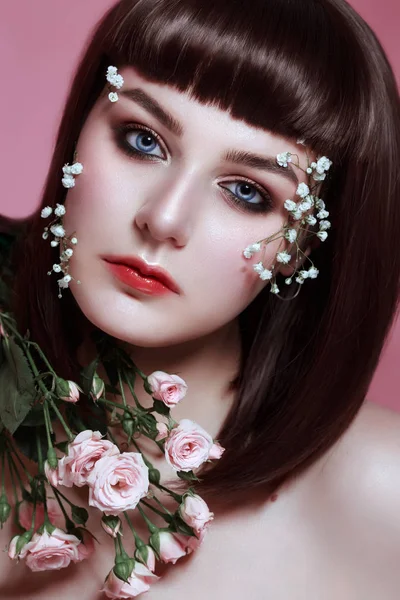 Портрет красивой молодой женщины с цветами на лице на прекрасном розовом фоне студии — стоковое фото