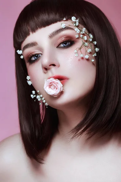 Portret van mooie jonge vrouw met bloemen op haar gezicht op de prachtige roze studio achtergrond — Stockfoto