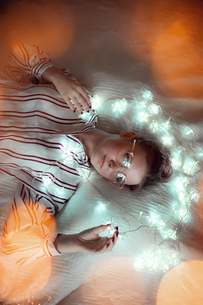 Young woman with fairy lights dreaming in bed — Stock Photo, Image