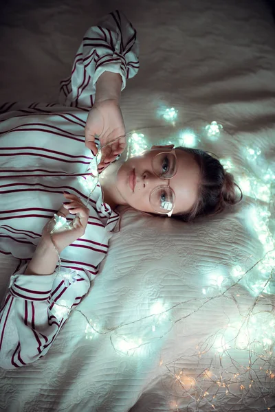 Fiatal nő álmodik az ágyban égősor — Stock Fotó