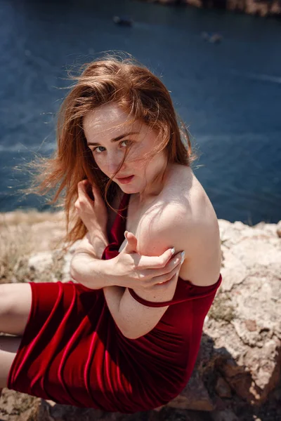 Een mooie roodharige vrouw zit op een rots — Stockfoto