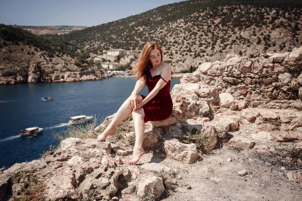 Eine schöne rothaarige Frau sitzt auf einem Felsen — Stockfoto