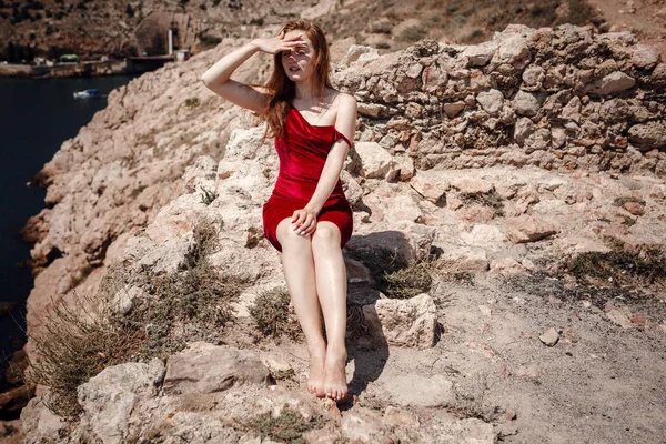 Eine schöne rothaarige Frau sitzt auf einem Felsen — Stockfoto