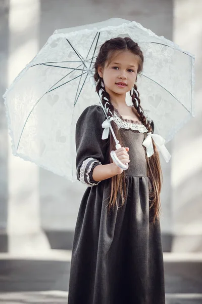 Mooi klein meisje in een oude jurk op de achtergrond van de architectuur van het historische centrum — Stockfoto