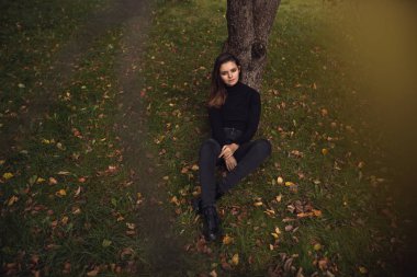 Güzel bir genç esmer siyah bir kazak ve ceket sonbahar Parkı boyunca yürür,