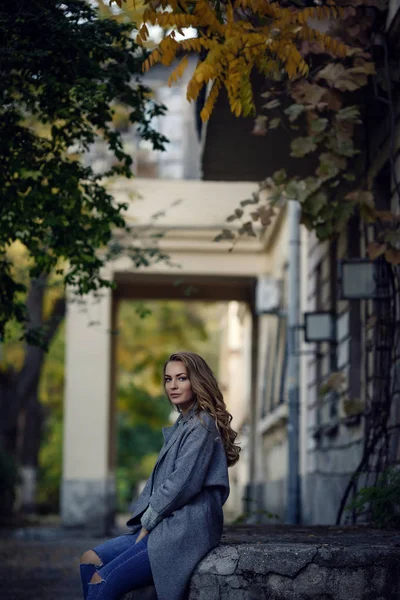 Fashion model wearing ripped boyfriend jeans, jacket and sneakers posing in the city — Stock Photo, Image