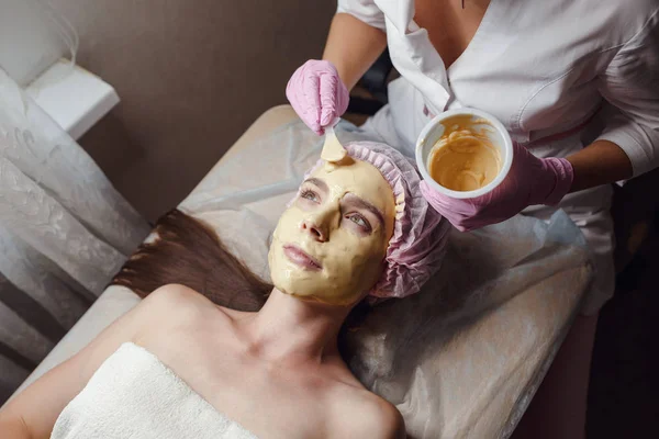 Cosmetologist doing beauty procedure for patient. Peeling Gold Mask