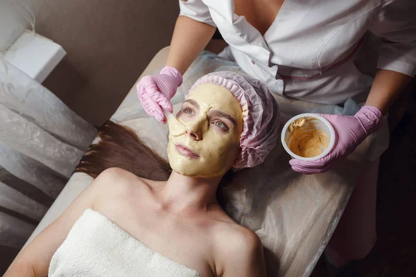 Cosmetologist doing beauty procedure for patient. Peeling Gold Mask