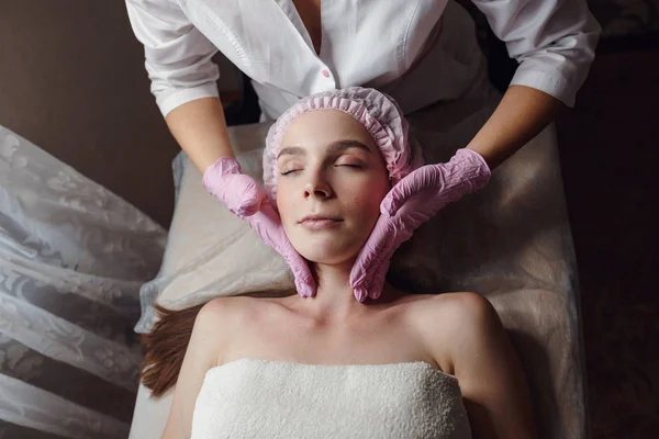 Cosmetología sala, esteticista hace masaje facial a una joven hermosa chica — Foto de Stock