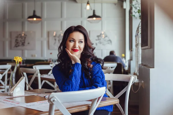 La mujer en el café se sienta en una mesa, bebe café y mira a la ventana — Foto de Stock