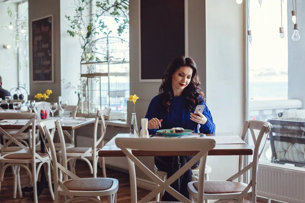 De vrouw in het café zit aan een tafel, drinkt koffie en kijkt naar Window — Stockfoto