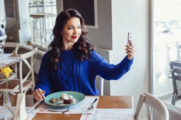 La mujer en el café se sienta en una mesa, bebe café y mira a la ventana — Foto de Stock