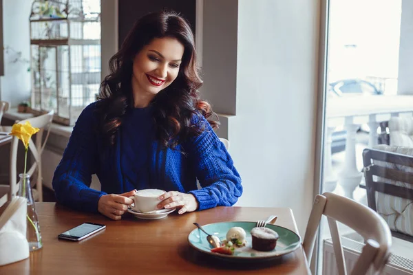 La mujer en el café se sienta en una mesa, bebe café y mira a la ventana — Foto de Stock