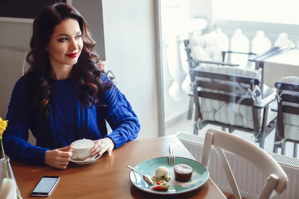 La mujer en el café se sienta en una mesa, bebe café y mira a la ventana —  Fotos de Stock