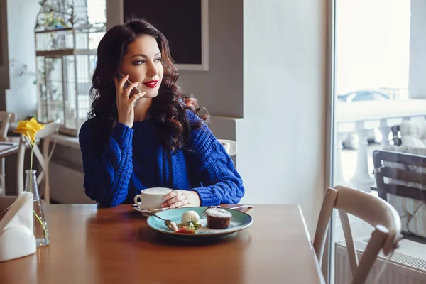 La mujer en el café se sienta en una mesa, bebe café y mira a la ventana —  Fotos de Stock