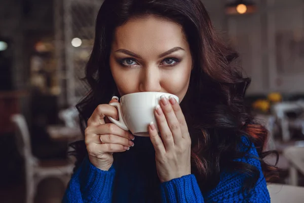 A nő a kávézóban ül egy asztalhoz, iszik kávét, és úgy néz ki ablak — Stock Fotó