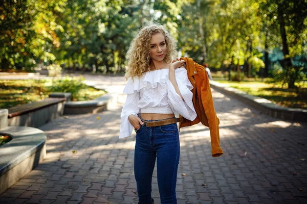 Eine schöne junge Frau mit blonden Locken spaziert durch die sonnige Stadt — Stockfoto