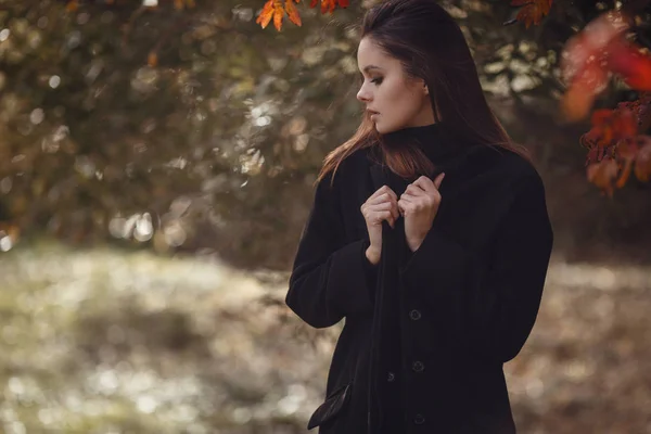 Eine schöne junge Brünette spaziert in schwarzem Pullover und Mantel durch den herbstlichen Park, — Stockfoto