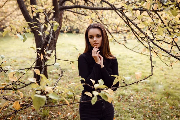 Uma bela jovem morena caminha pelo parque de outono com uma camisola preta e um casaco , — Fotografia de Stock