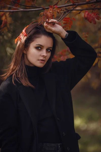 Uma bela jovem morena caminha pelo parque de outono com uma camisola preta e um casaco , — Fotografia de Stock