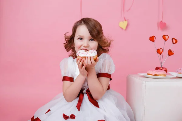 Pembe arka planda elinde donut olan küçük bir kızın portresi — Stok fotoğraf