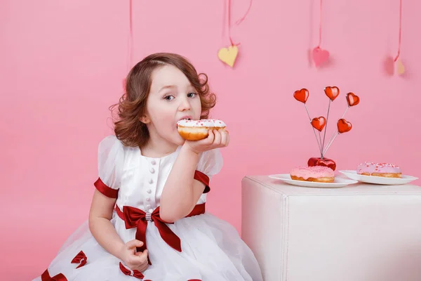 Portret van een klein meisje met een donut in haar handen op roze achtergrond — Stockfoto