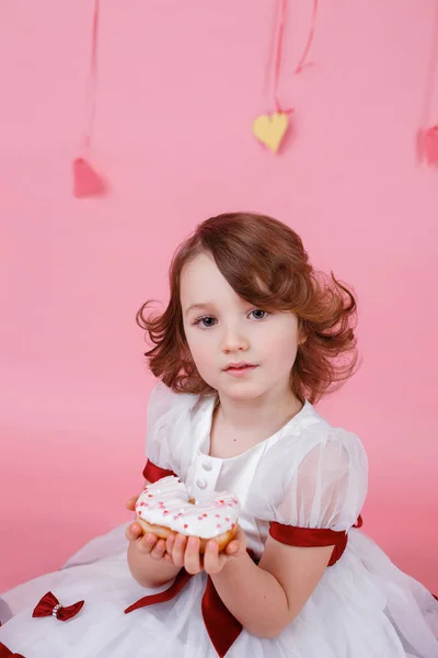 Portrait of a little girl with a donut in her hands on pink background — Stock Photo, Image