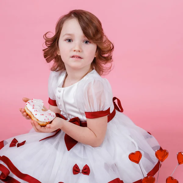 Retrato de uma menina com um donut nas mãos sobre fundo rosa — Fotografia de Stock