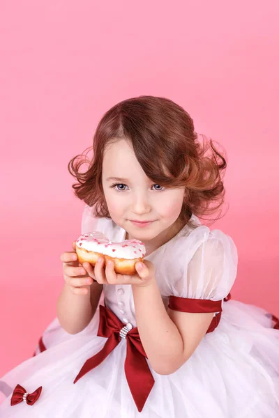 Retrato de uma menina com um donut nas mãos sobre fundo rosa — Fotografia de Stock