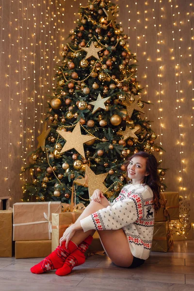 Una bella giovane donna con un maglione bianco è seduta vicino all'albero di Capodanno — Foto Stock