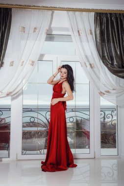 Kırmızı elbiseli muhteşem bir kadın otel süitinde duruyor.