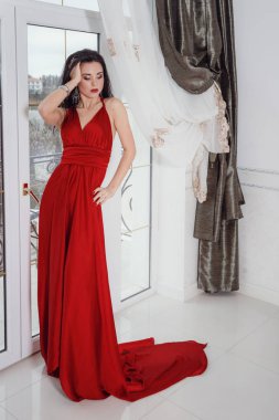 Kırmızı elbiseli muhteşem bir kadın otel süitinde duruyor.