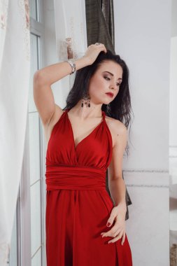 Kırmızı elbiseli muhteşem bir kadın otel süitinde duruyor.