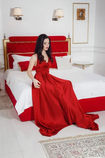 Seducente donna in abito rosso rilassante su un divano in interni di lusso — Foto Stock