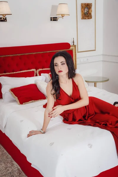 Mujer atractiva en vestido rojo relajante en un sofá en el interior de lujo — Foto de Stock