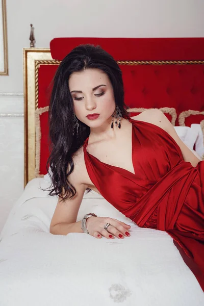 Verleidelijke vrouw in rode jurk ontspannen op een sofa in luxe interieur — Stockfoto