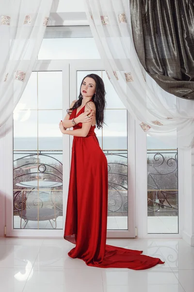 Nádherná žena v červených šatech stojí v hotelovém apartmá — Stock fotografie