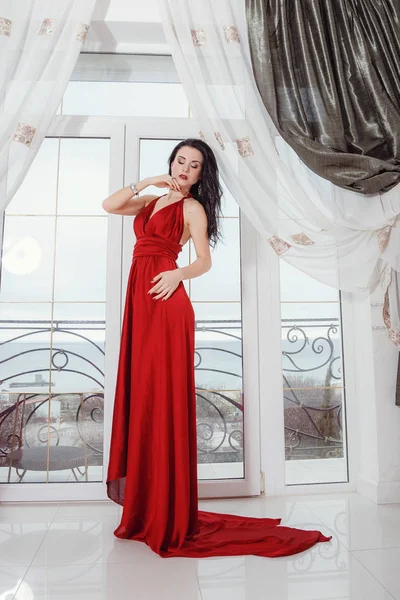 Nádherná žena v červených šatech stojí v hotelovém apartmá — Stock fotografie