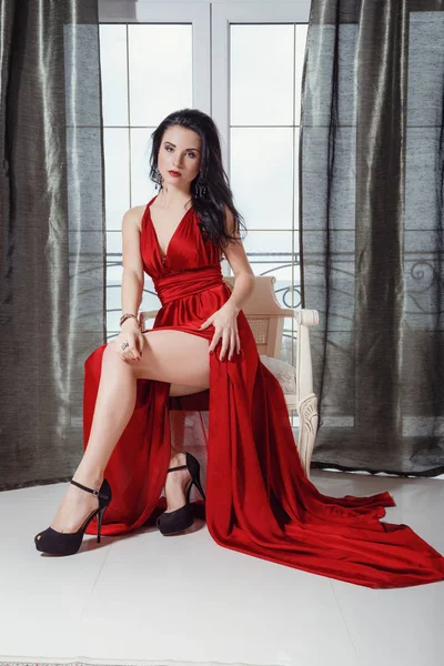 Sexy glamour mulher com cabelo preto no elegante vestido vermelho sentado na poltrona — Fotografia de Stock
