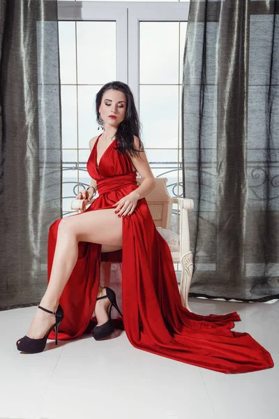 Sexy mujer glamour con pelo negro en elegante vestido rojo sentado en el sillón — Foto de Stock