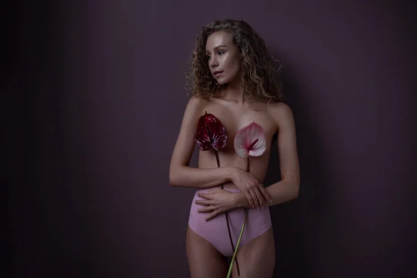 Tender portrait of a woman with curly hair in a room. red and pink callas cover the model chest. idea and concept of femininity, tenderness, spring and sexuality