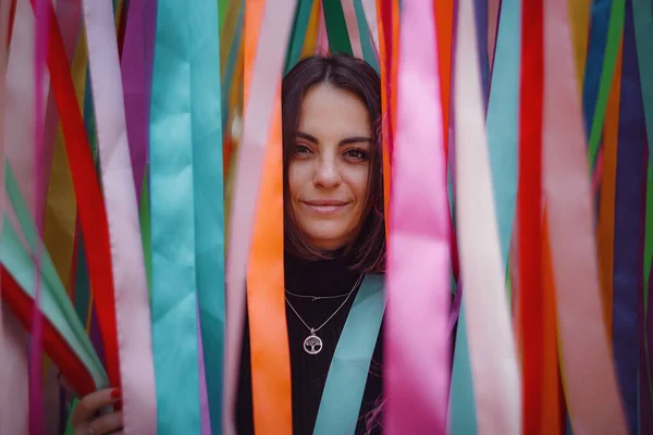 Beautiful young brunette woman walks in Moscow. Feeling happy in big city. unusual installation of colorful ribbons during a seasonal festival in the city